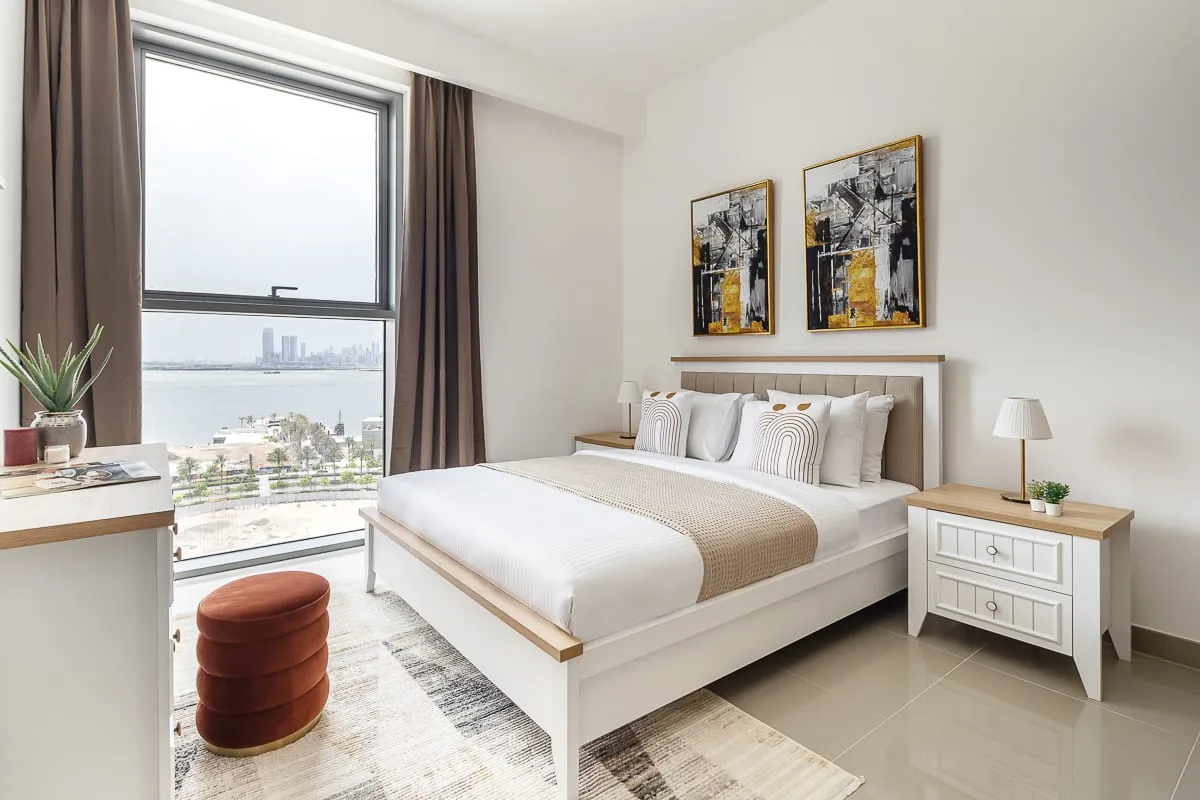 Un dormitorio luminoso con una cama bien tendida junto a una ventana grande.