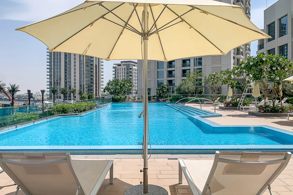 Una piscina al aire libre está enmarcada por una sombrilla grande y asientos cercanos.