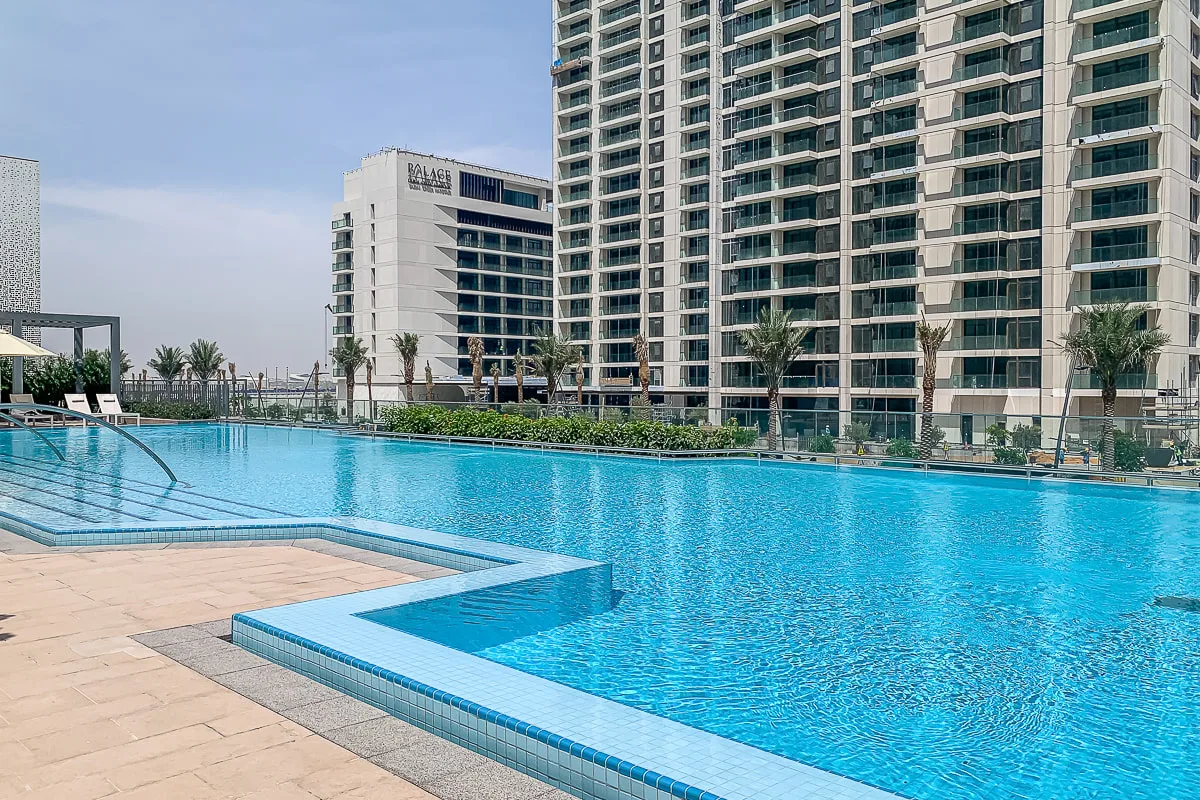 Una piscina al aire libre está junto a una terraza pavimentada y edificios altos.