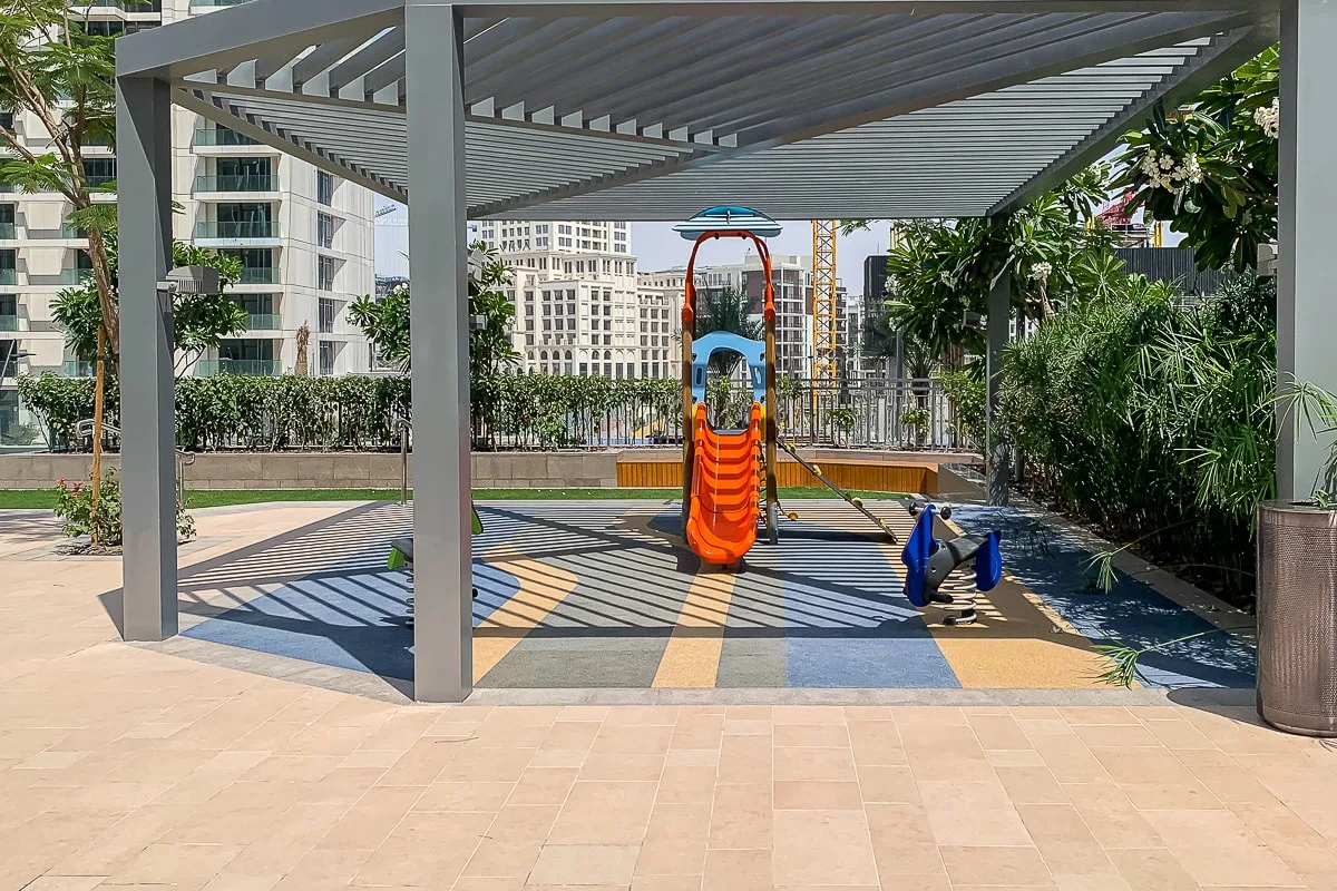 Un parque infantil al aire libre con sombra, un tobogán colorido y una estructura para trepar.