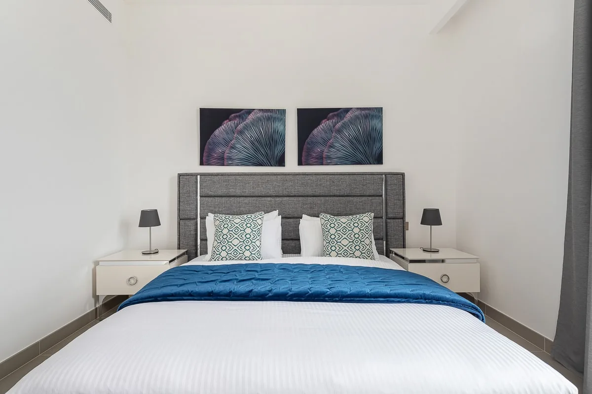 Un dormitorio con una cama bien tendida y dos cuadros sobre el cabecero.