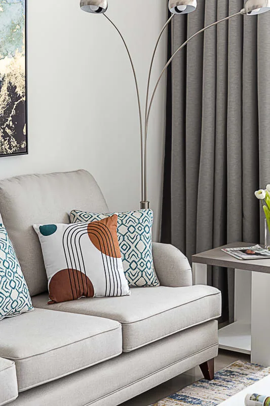 Una zona de estar con cojines estampados junto a una lámpara de pie y cortinas.