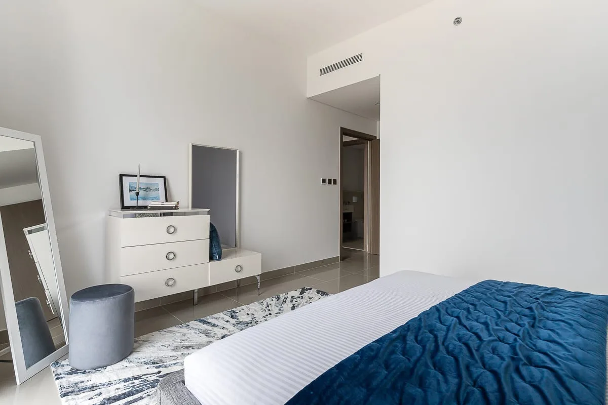 Un dormitorio con una cama, una manta azul y una cómoda blanca.