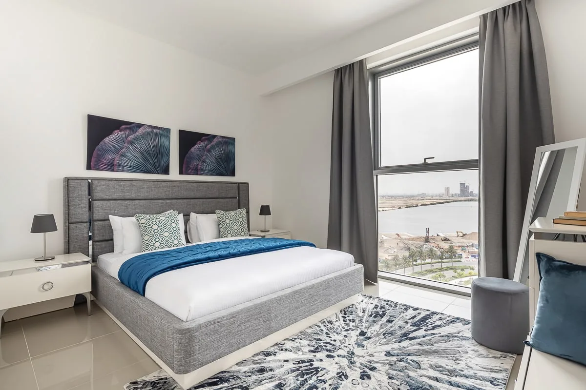 Un dormitorio luminoso con una cama, cortinas grises y una ventana grande.