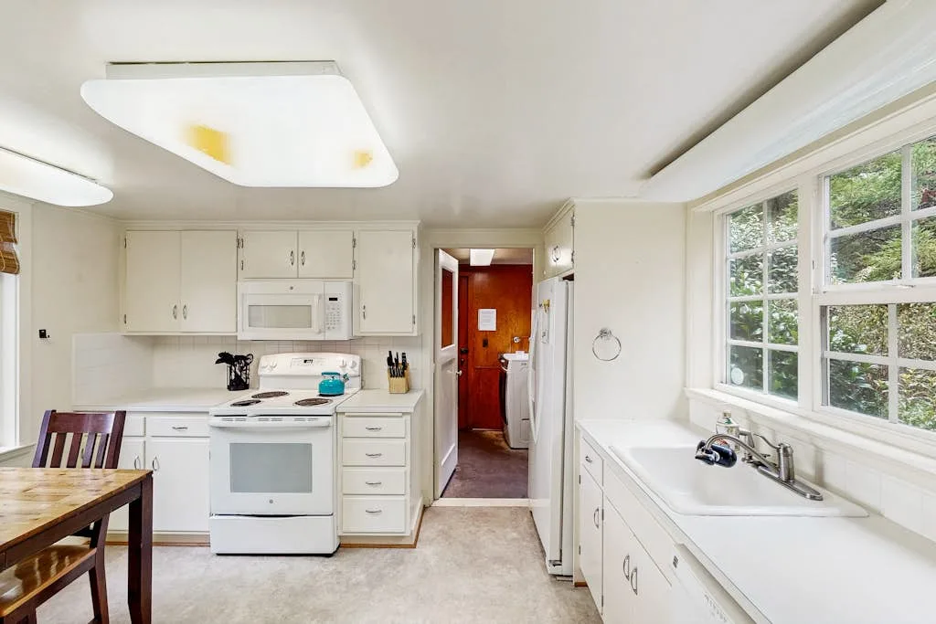 A bright kitchen with white cabinets, a stove, and a long sink counter.