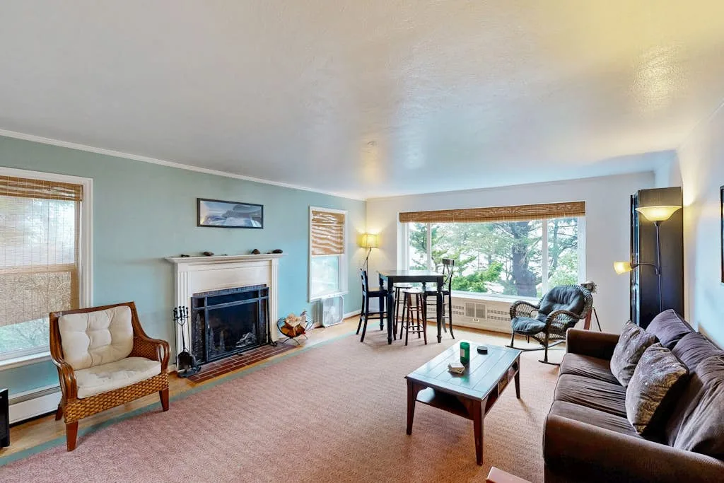 A living room with seating, a fireplace, and a dining table beside large windows.