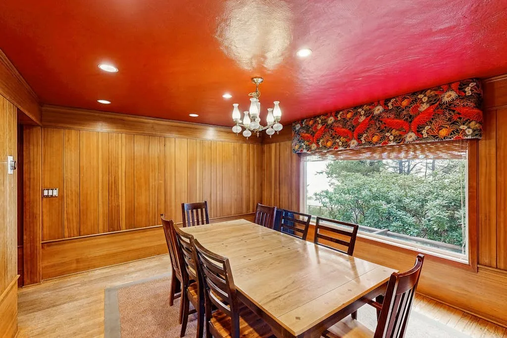 A wood-paneled dining room with a long table beside a large window.