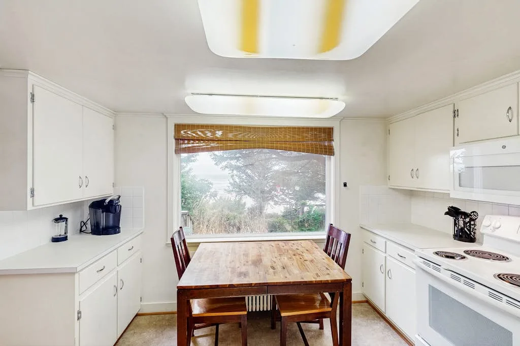 A bright kitchen with a wooden dining table beside a large window.