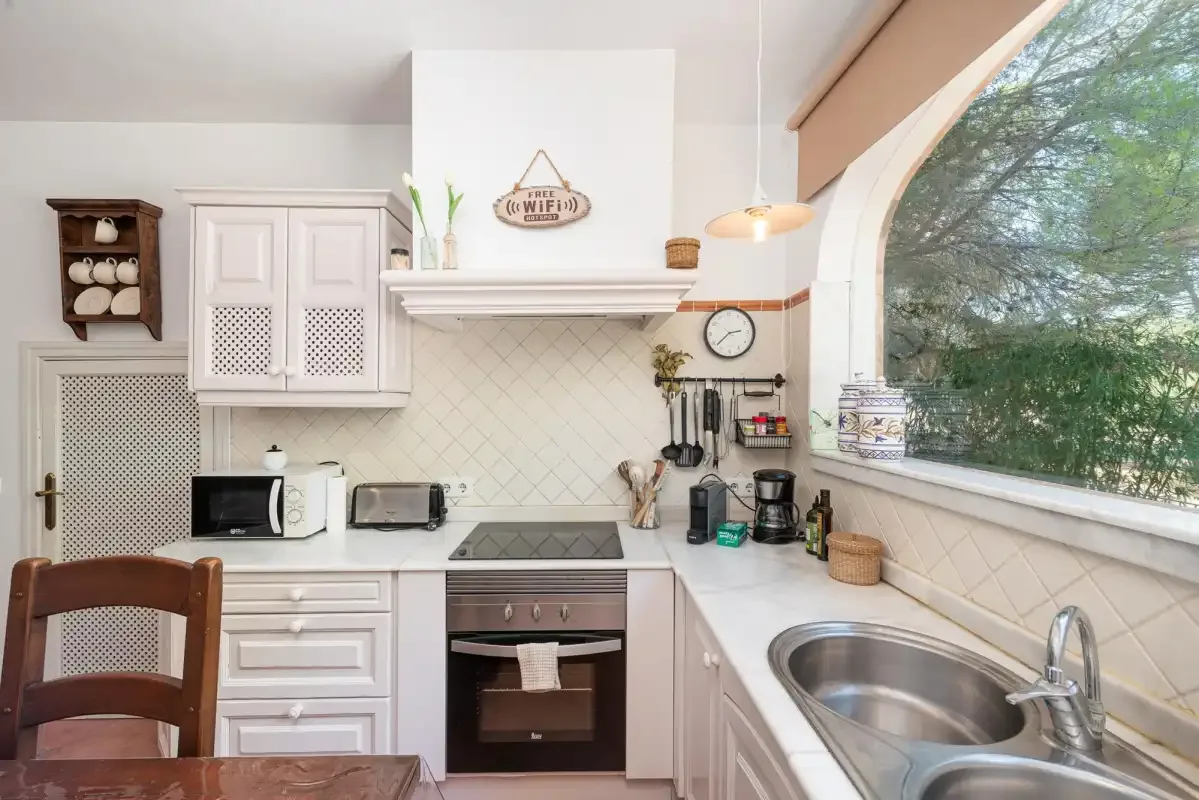 A bright kitchen with white cabinets, a cooktop, and a sink beneath a large window.
