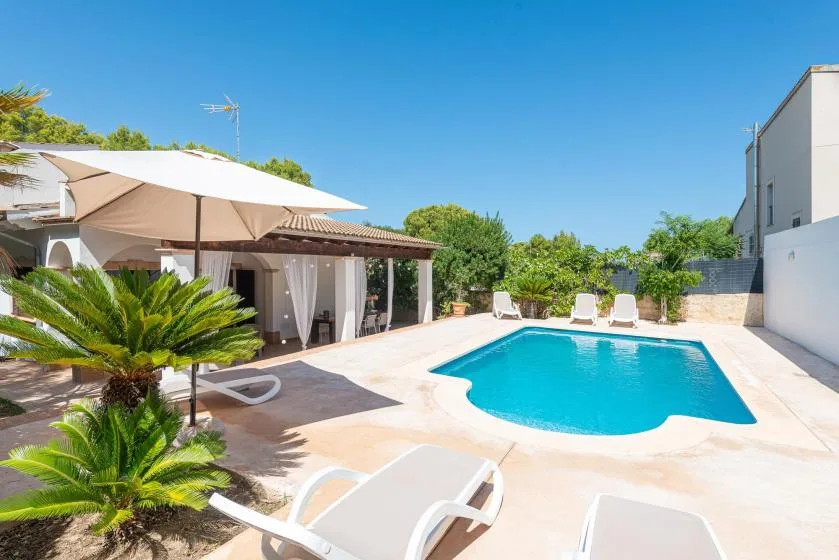 An outdoor swimming pool sits beside a shaded patio with loungers.
