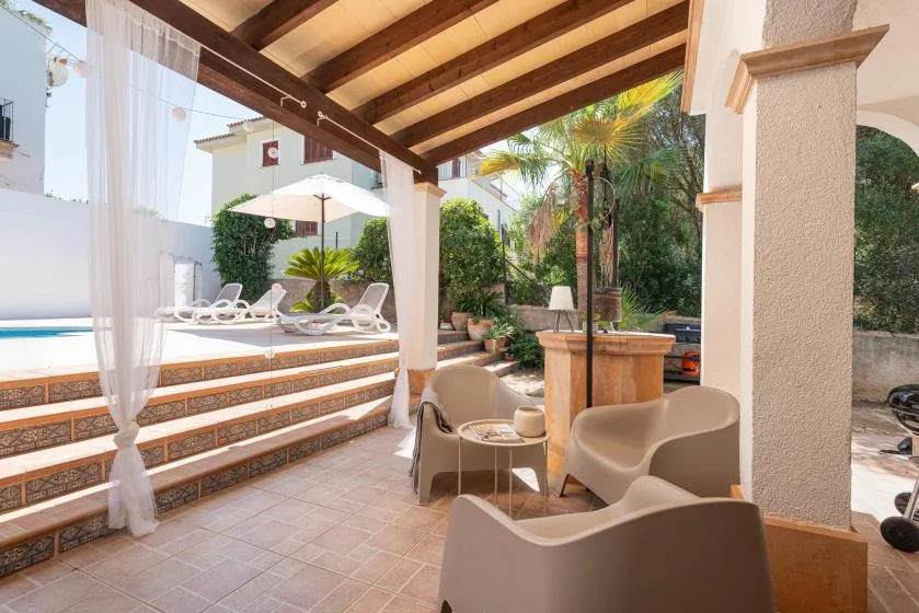 A covered patio seating area overlooks a pool and a lush garden.