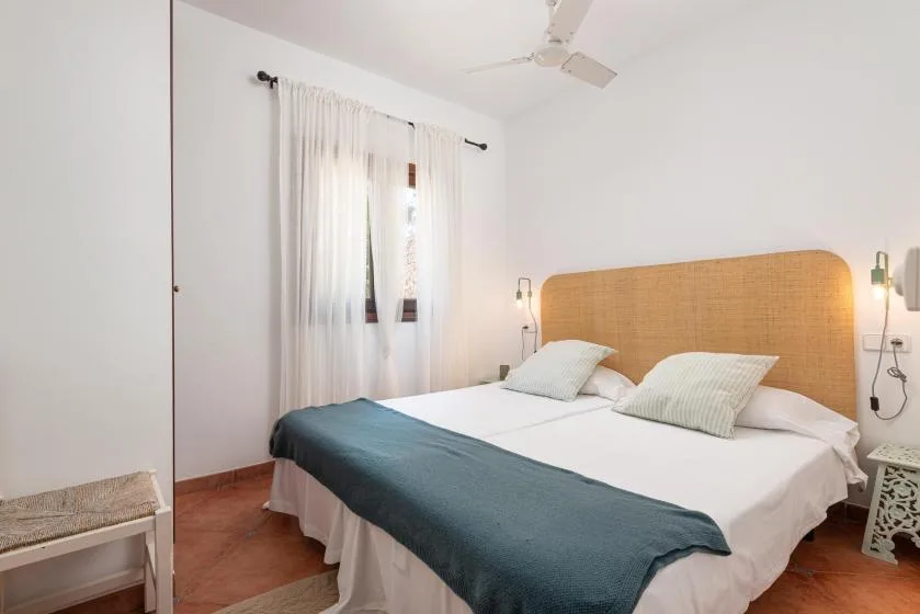 A bright bedroom with a bed beneath a woven headboard and a curtained window.