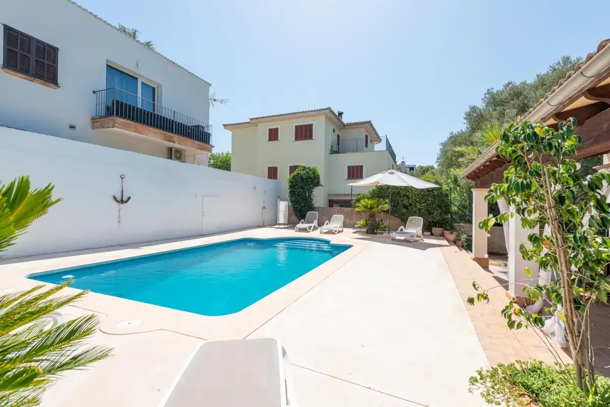 An outdoor swimming pool sits beside a paved patio with seating.