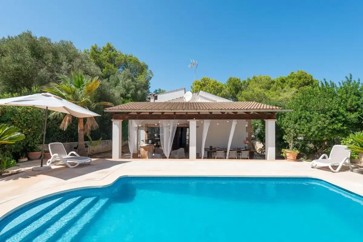 A swimming pool and patio sit in front of a covered outdoor seating area.