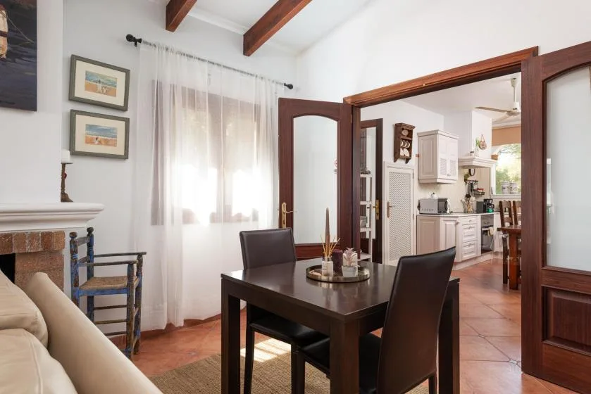 A dining area opens through wooden doors into a bright kitchen.