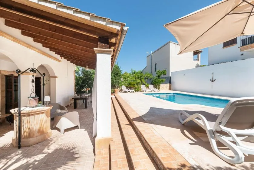 A sunny patio beside a swimming pool, with shaded seating and a canopy.