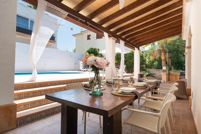 A covered patio dining area overlooks a pool, with a table set for a meal.