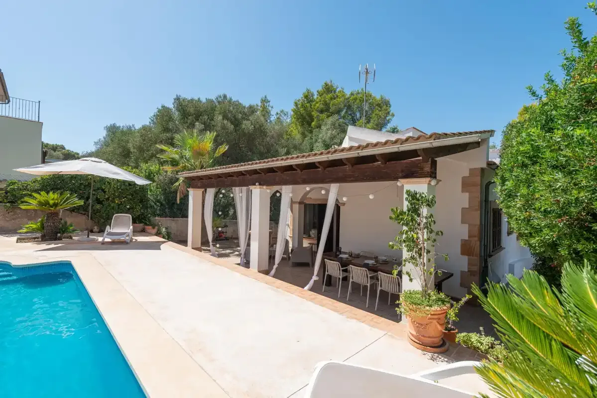 A swimming pool and covered patio sit beside a garden.