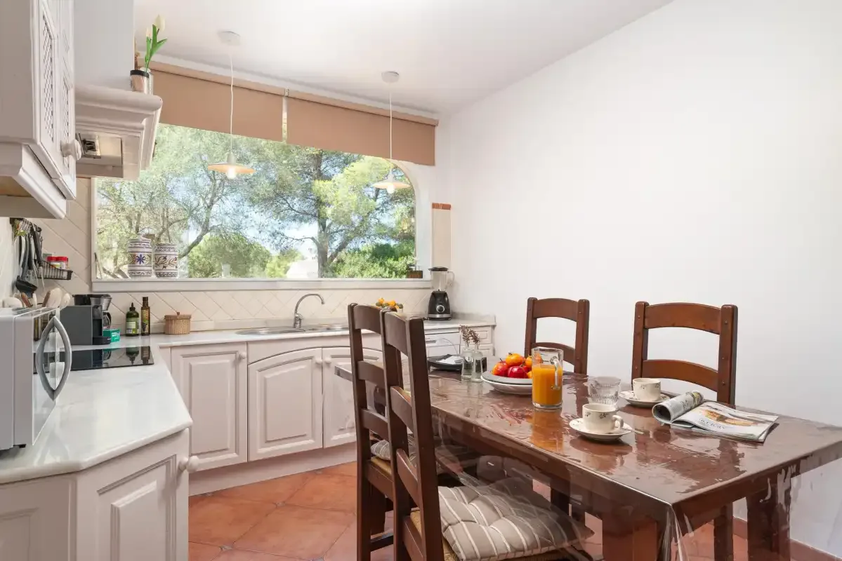 A kitchen and dining area with a wooden table beside a large window.