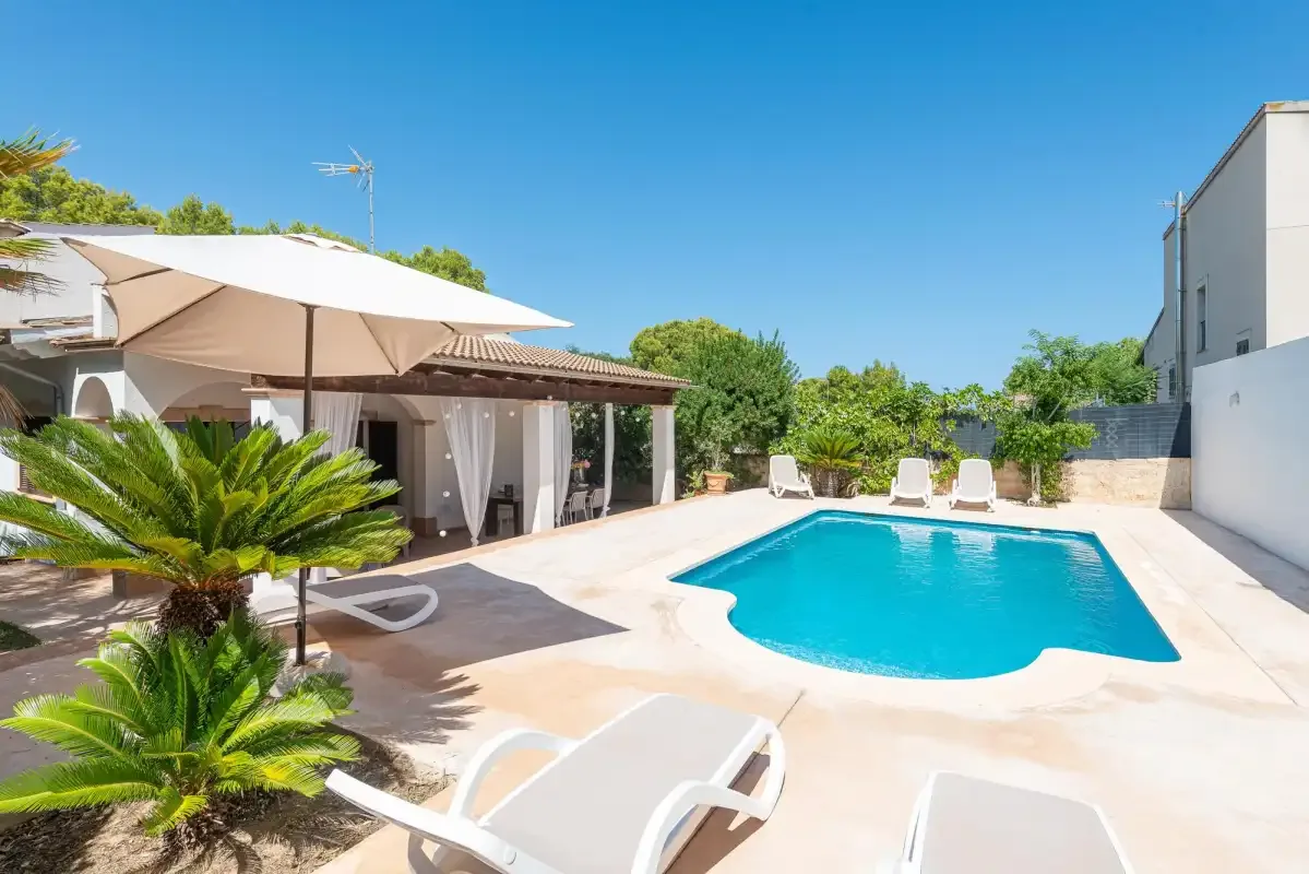 A sunny outdoor pool area with lounge chairs, patio seating, and a large shade umbrella.