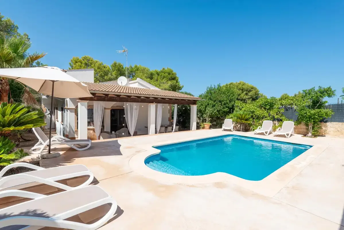 An outdoor swimming pool beside a single-story house and several loungers.