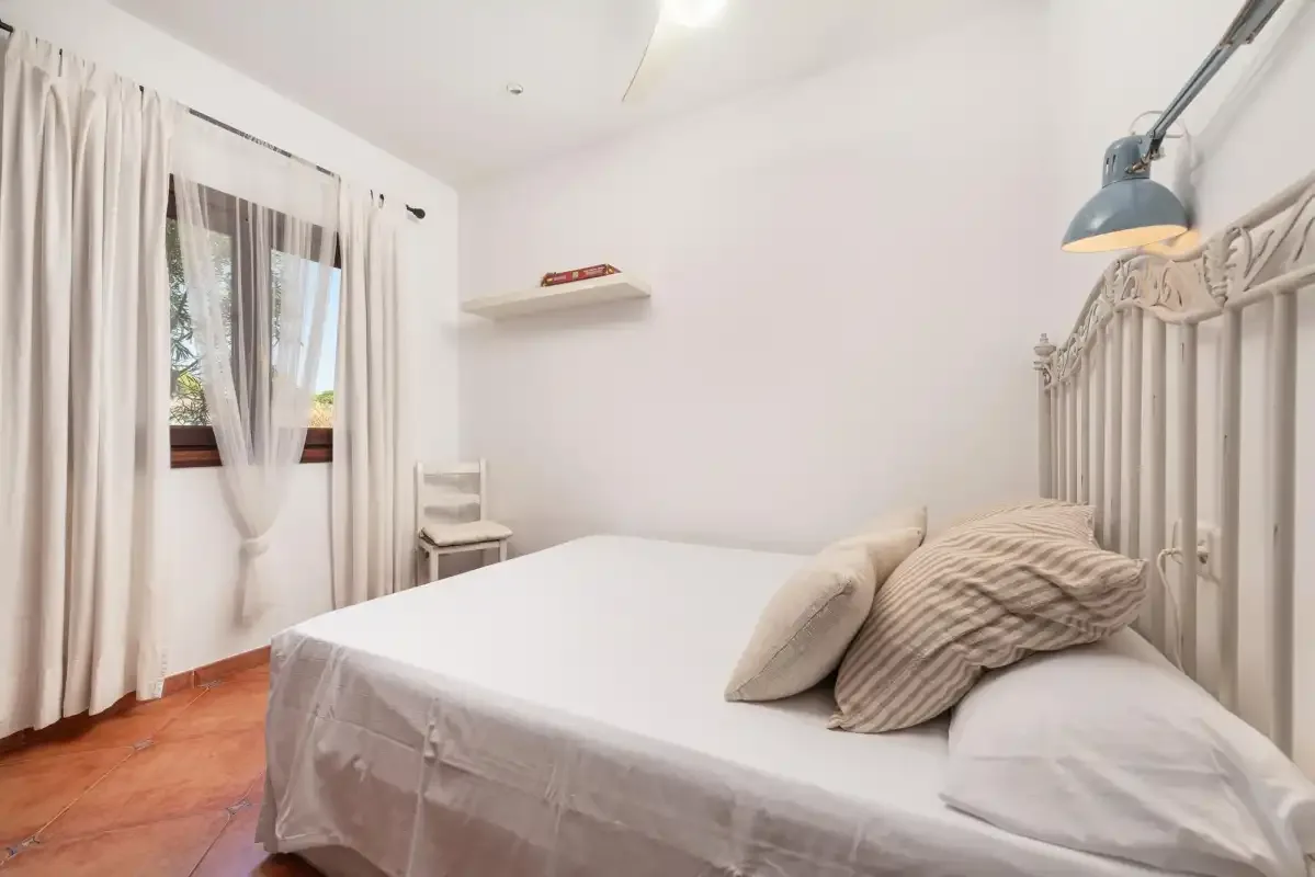 A bright bedroom with a bed, striped pillows, and a curtained window.