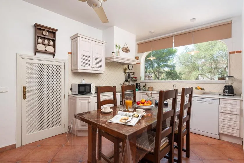 A kitchen dining area with a wooden table and a wide window overlooking trees.