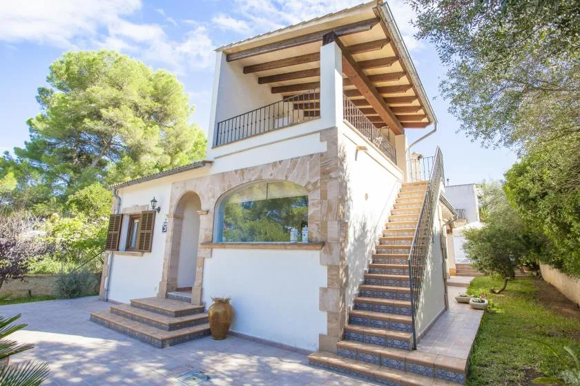 A two-story house with an exterior staircase stands among trees.