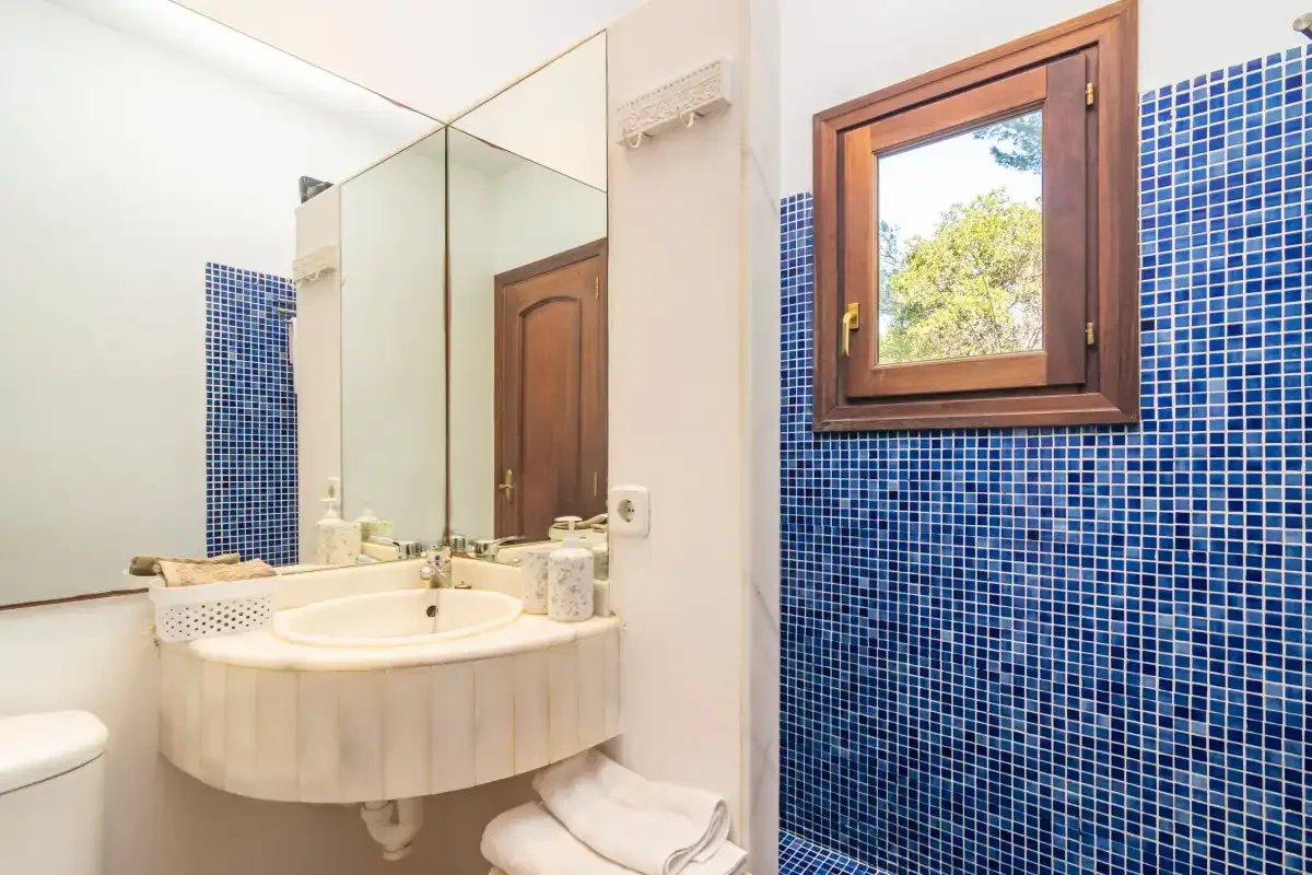 A bathroom with a curved sink beneath a mirror and a wooden-framed window.