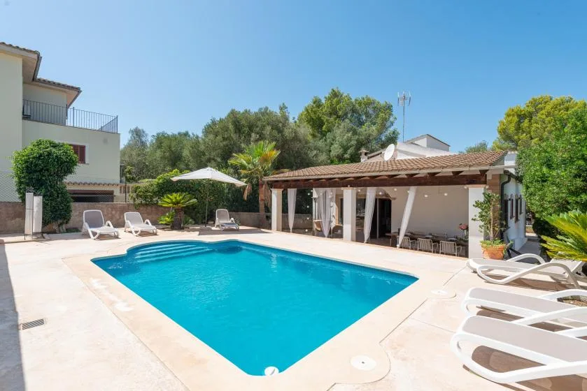 An outdoor swimming pool sits beside a shaded patio with lounge seating.