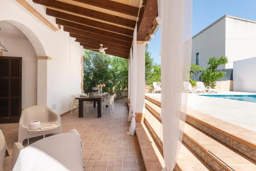 A covered patio with a dining table and seating overlooks a pool.