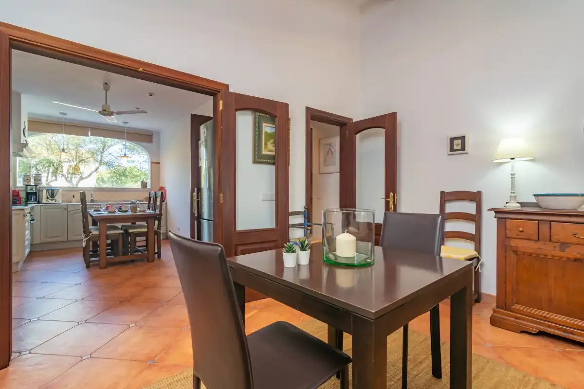 A dining area with a dark table and chairs opens onto a kitchen.