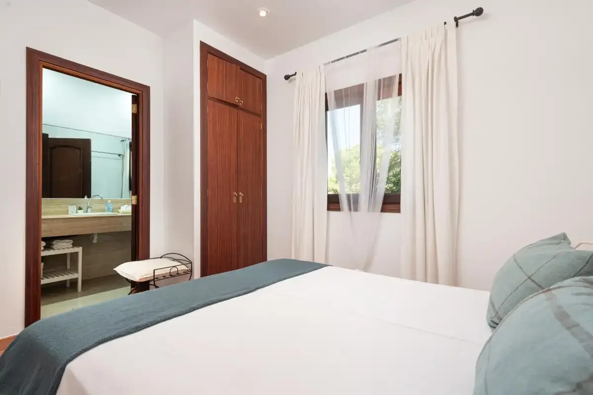 A bedroom with a neatly made bed and a window with sheer curtains.