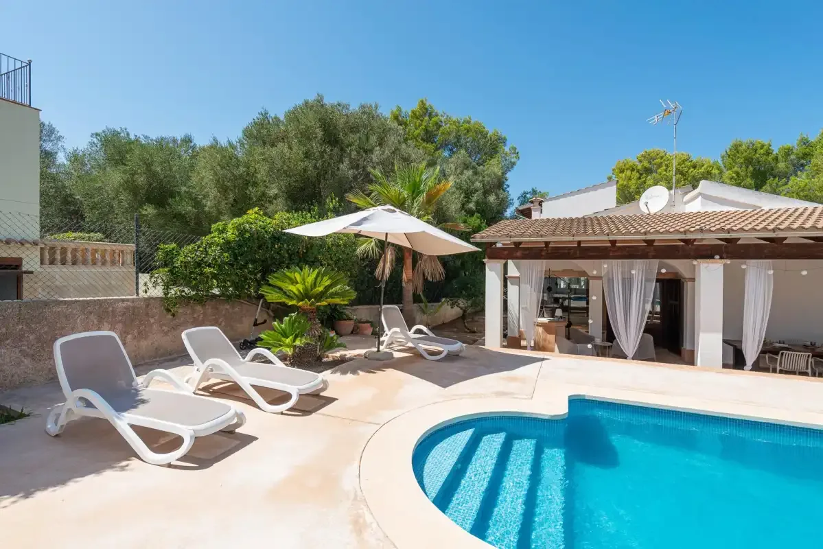 A swimming pool and sun loungers beside a patio with a shaded seating area.