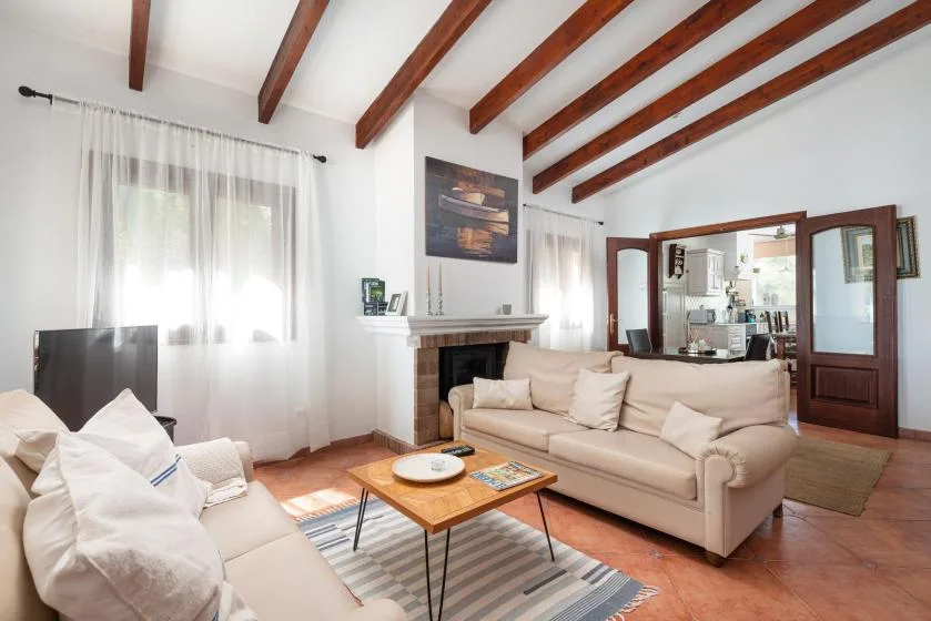 A bright living room with seating, a fireplace, and exposed wooden ceiling beams.