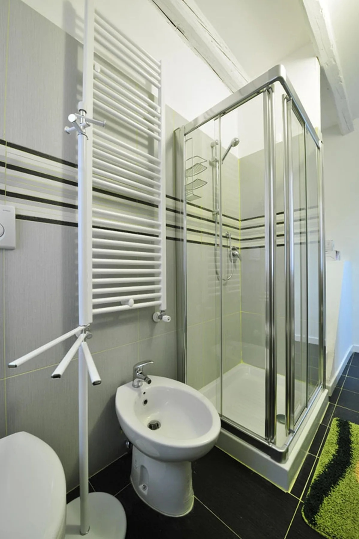 Un baño alicatado con ducha de vidrio, lavabo con pedestal y toallero mural.