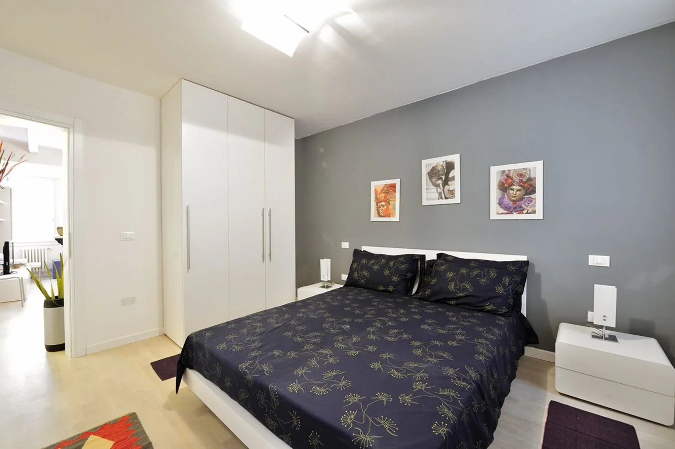 Un dormitorio con una cama de estampado oscuro y armarios blancos junto a una pared gris.