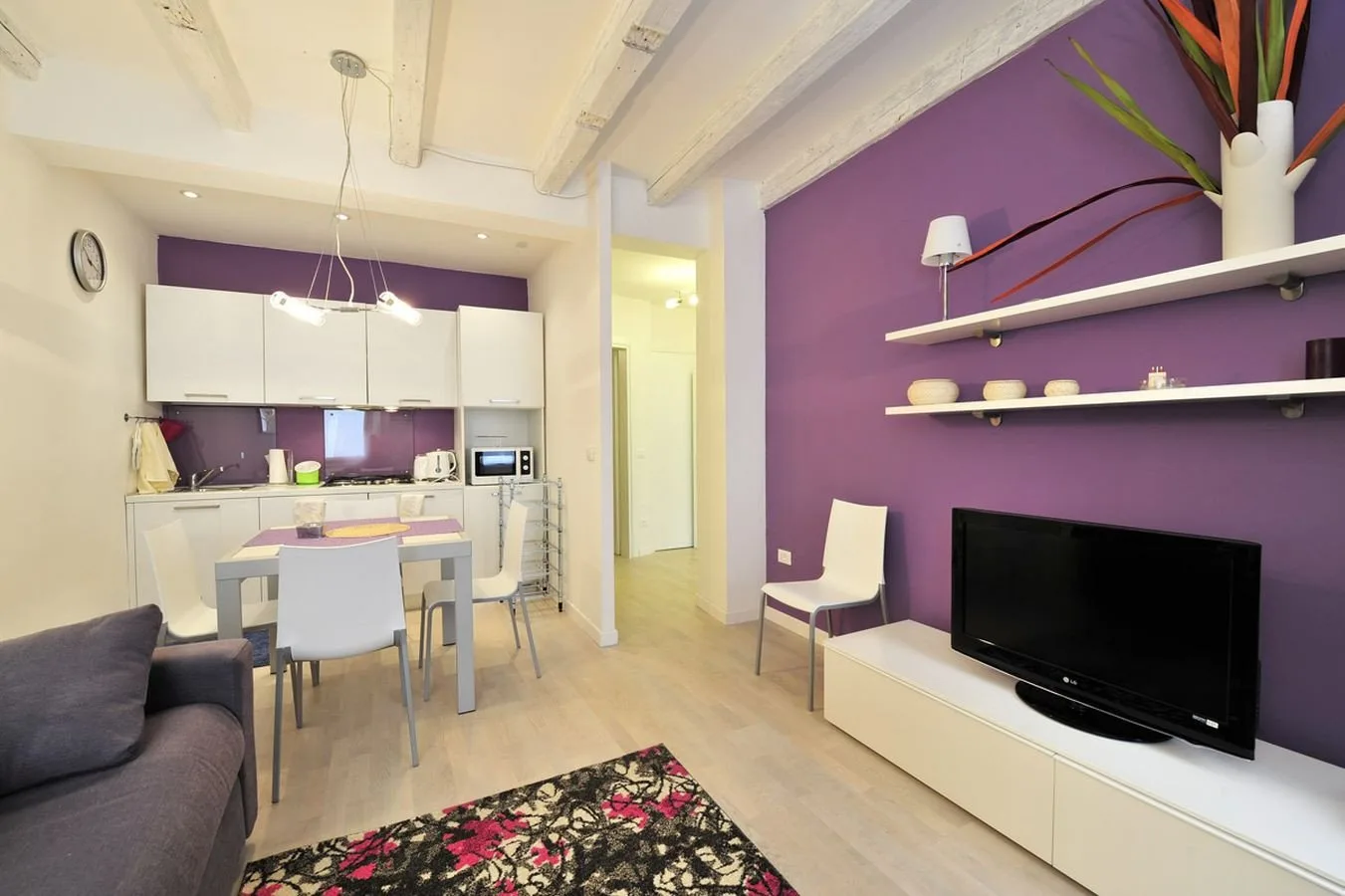 Una sala y comedor con televisor, mesa y una pared de acento morada.