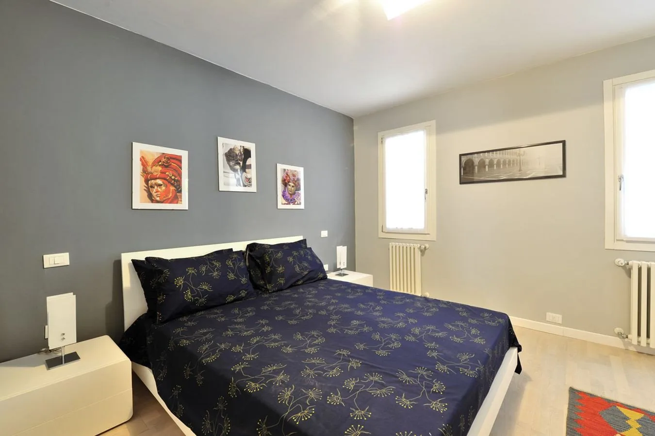 Un dormitorio con una cama cubierta con ropa de cama oscura estampada y cuadros en la pared.