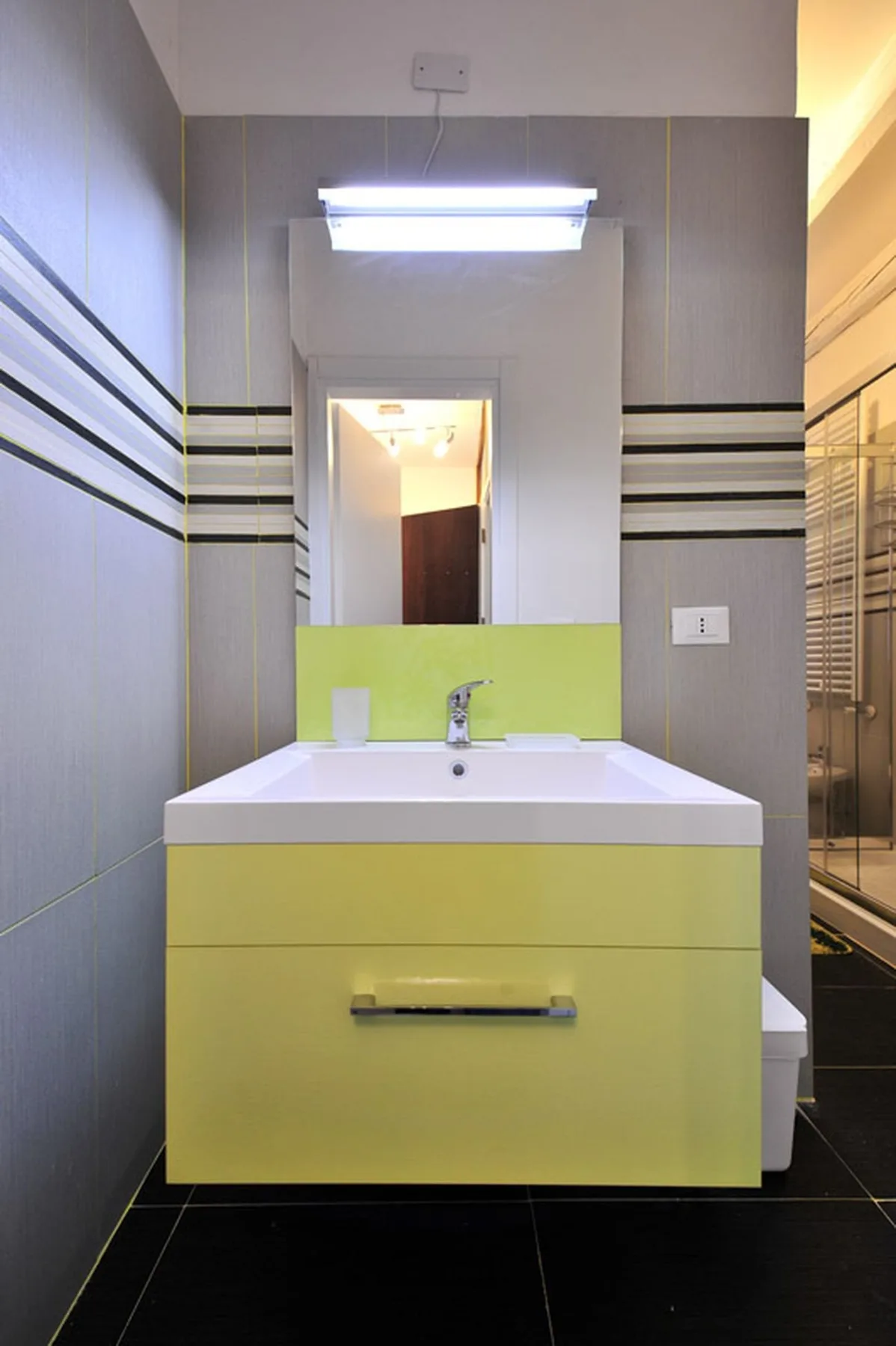 Un mueble de baño con lavabo y espejo está frente a paredes revestidas de azulejos.