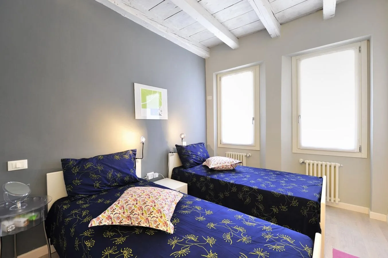 Un dormitorio con dos camas cubiertas con ropa de cama azul estampada y ventanas luminosas.
