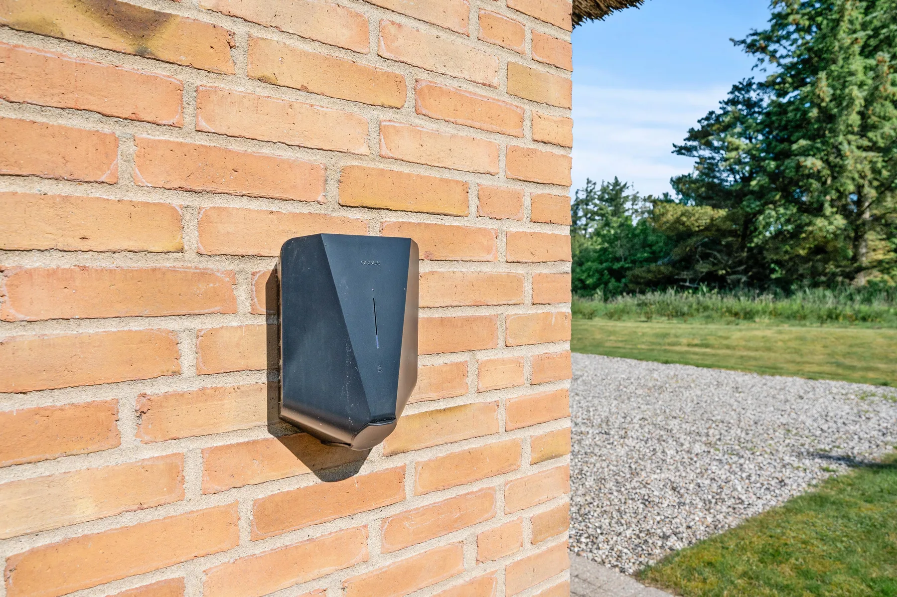 Una pared exterior de ladrillo con una lámpara oscura junto a un camino de grava.