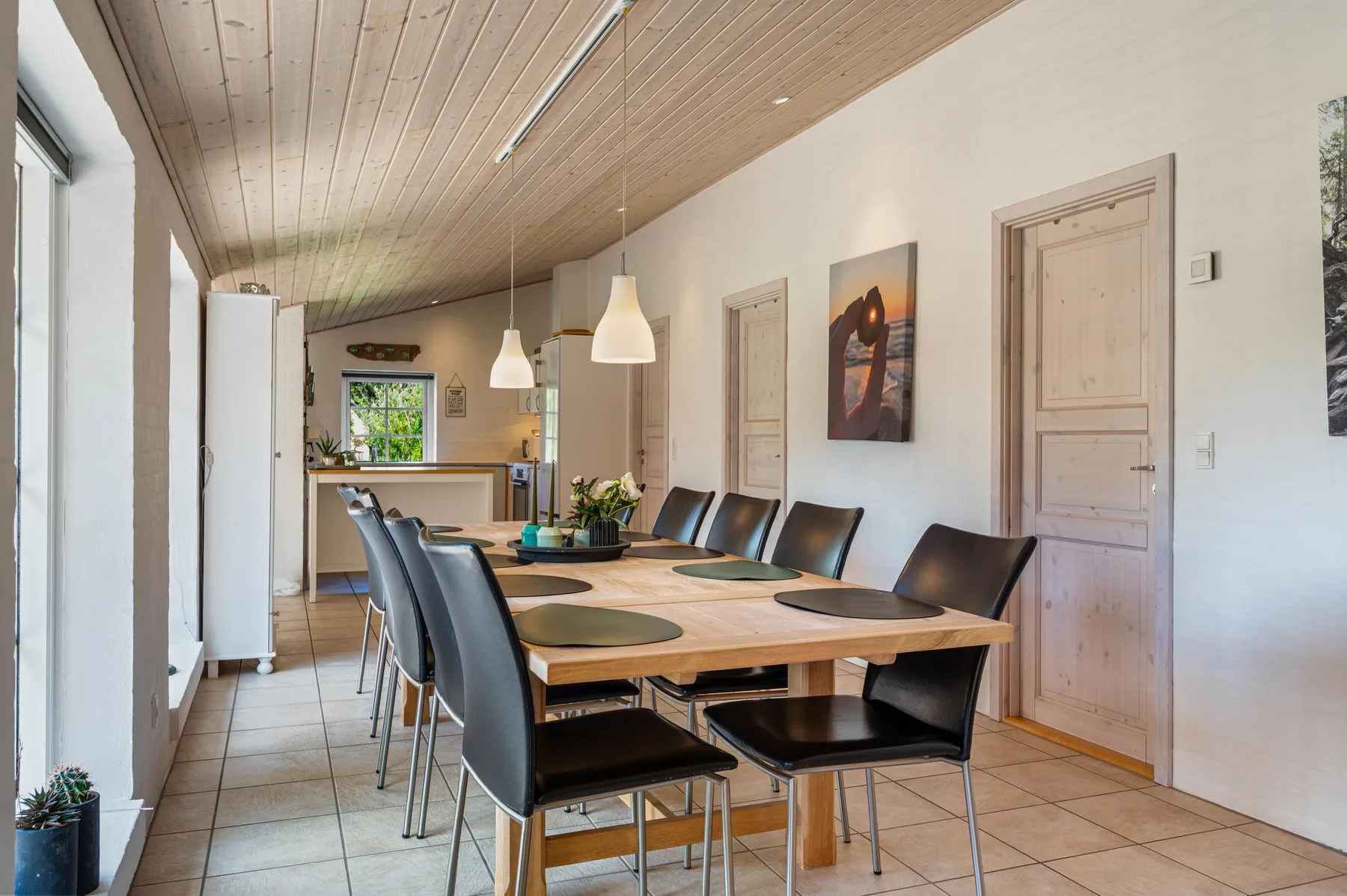 Comedor con una mesa larga y asientos oscuros junto a una cocina.