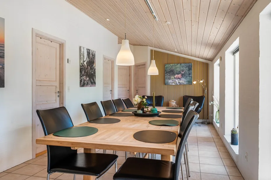 Un comedor con una mesa larga de madera y sillas bajo lámparas colgantes.