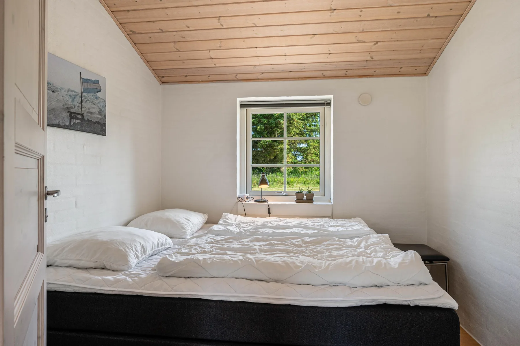 Un dormitorio con una cama bajo un techo de madera y una ventana con vistas a la vegetación.