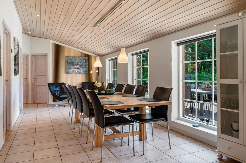 Comedor con una mesa larga, asientos y ventanas que dan a un jardín.