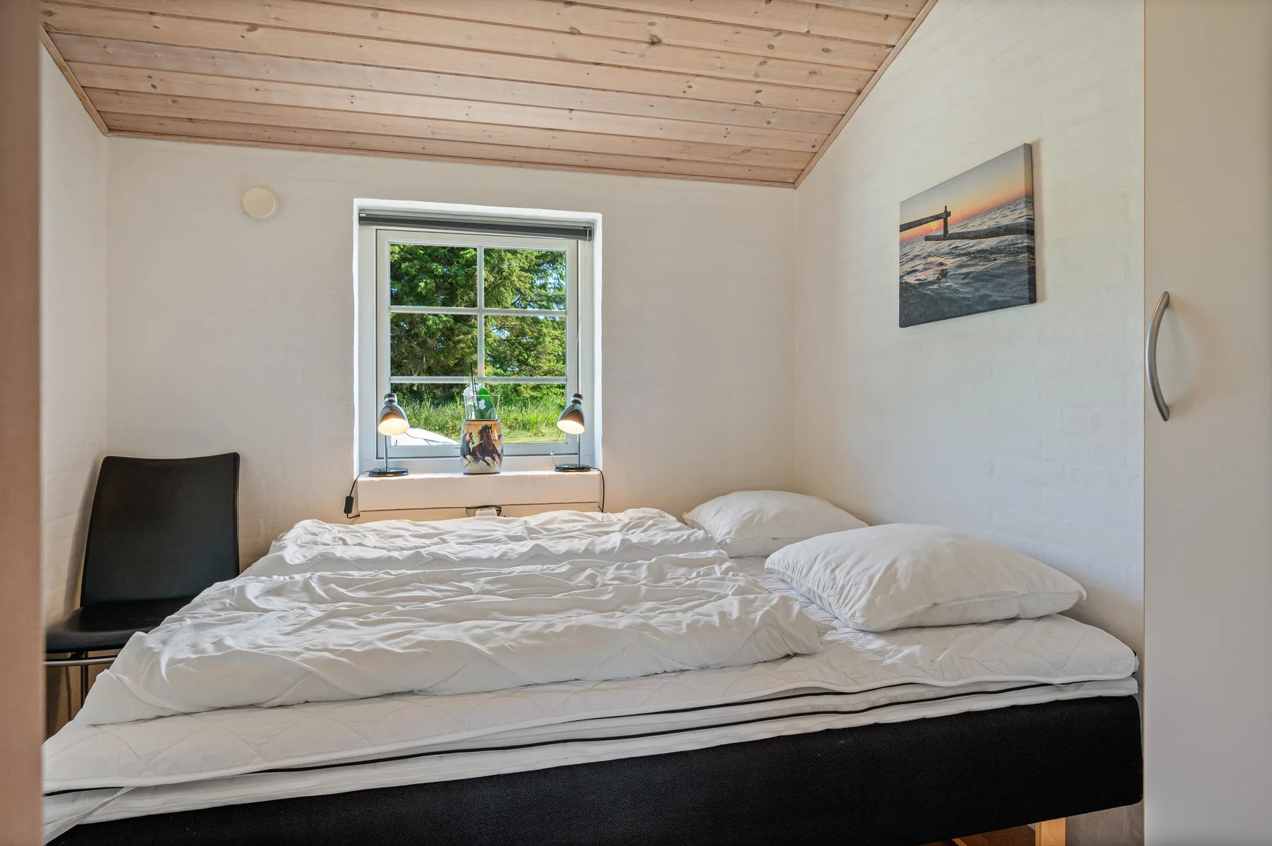 Un dormitorio con una cama bajo una ventana con vistas a la vegetación.