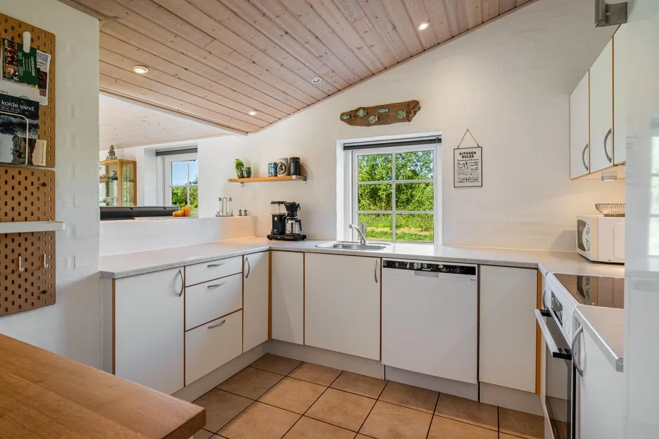 Una cocina luminosa con armarios blancos, una encimera y una ventana con vistas a la vegetación.