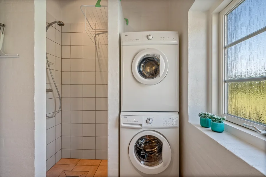 Un baño con ducha de azulejos y lavadoras apiladas.