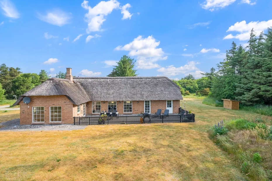 Una casa de ladrillo con techo de paja se alza en un paisaje de pradera abierta.